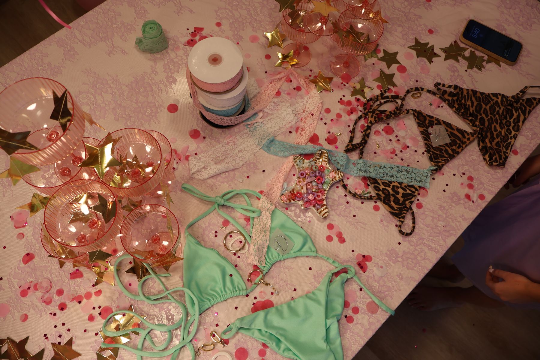 Mint and leopard bikini pieces laid out on a pink table with confetti